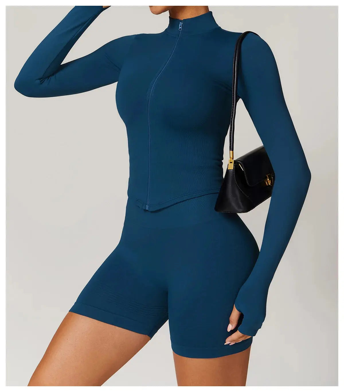 A person wears the Mirèlle Workout Jacket with Zip & Quick Dry in blue, paired with matching bike shorts and holding a small black shoulder bag. Face is not visible.