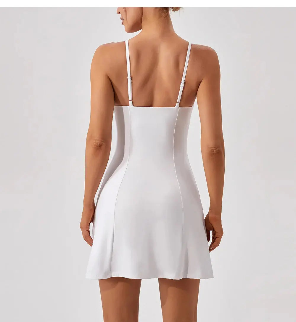 A woman is seen from behind wearing the Mirèlle Tennis Dress Triangle Top—a sleeveless, white, fitted dress with thin adjustable straps and built-in shorts—posed against a plain light background.