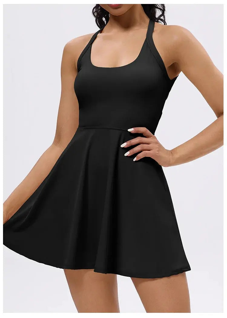 A woman models the Mirèlle Tennis Dress with Back Twist, a sleeveless black dress featuring a flared skirt and twist-back design, posing with one hand on her hip and the other holding out the skirt against a plain white background.